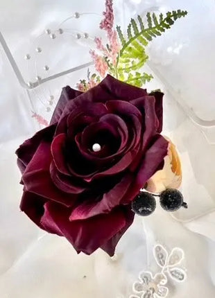 Close-up of a dark purple rose with green leaves on a white background