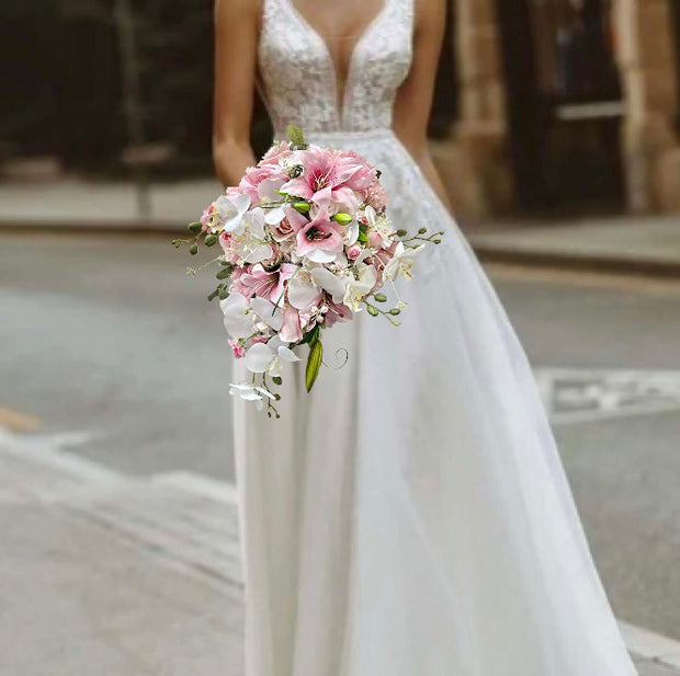 Bride in a white wedding dress holding a bouquet of pink and white flowers on a city street.