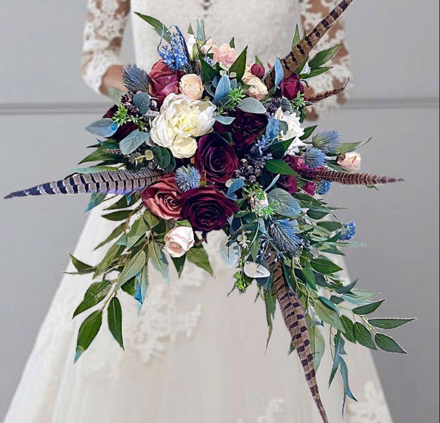 Bouquet with flowers and feathers held by a person wearing a white dress.