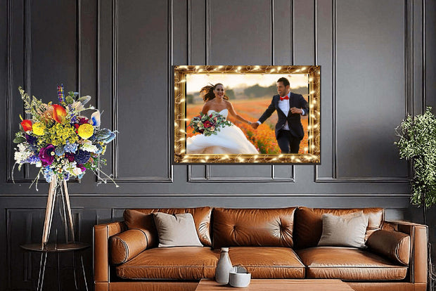 Decorative setup with a framed photograph of a couple, flowers, and a brown leather sofa against a dark paneled wall.