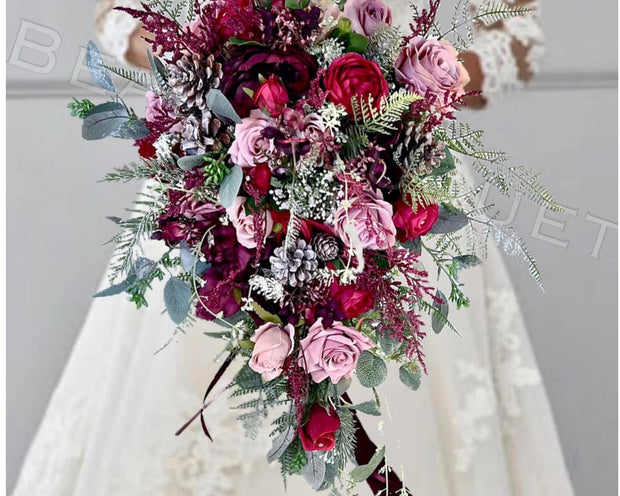 A cascading bridal bouquet with deep burgundy and pink roses, green eucalyptus, and white filler flowers, held by a person in a white lace wedding dress. The text 'Winters Love' is overlaid at the bottom.