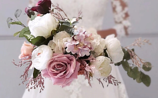 Bride holding large peony and rose bouquet in blush pinks, ivory and mave tones
