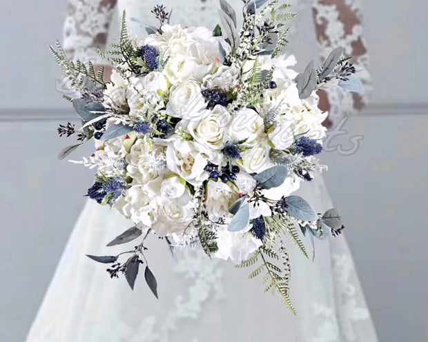 A bridal bouquet arrangement featuring white roses, blue berry accents, and green foliage, held in front of a white lace wedding dress. The text 'This Magic Moment' is written in blue script at the bottom.