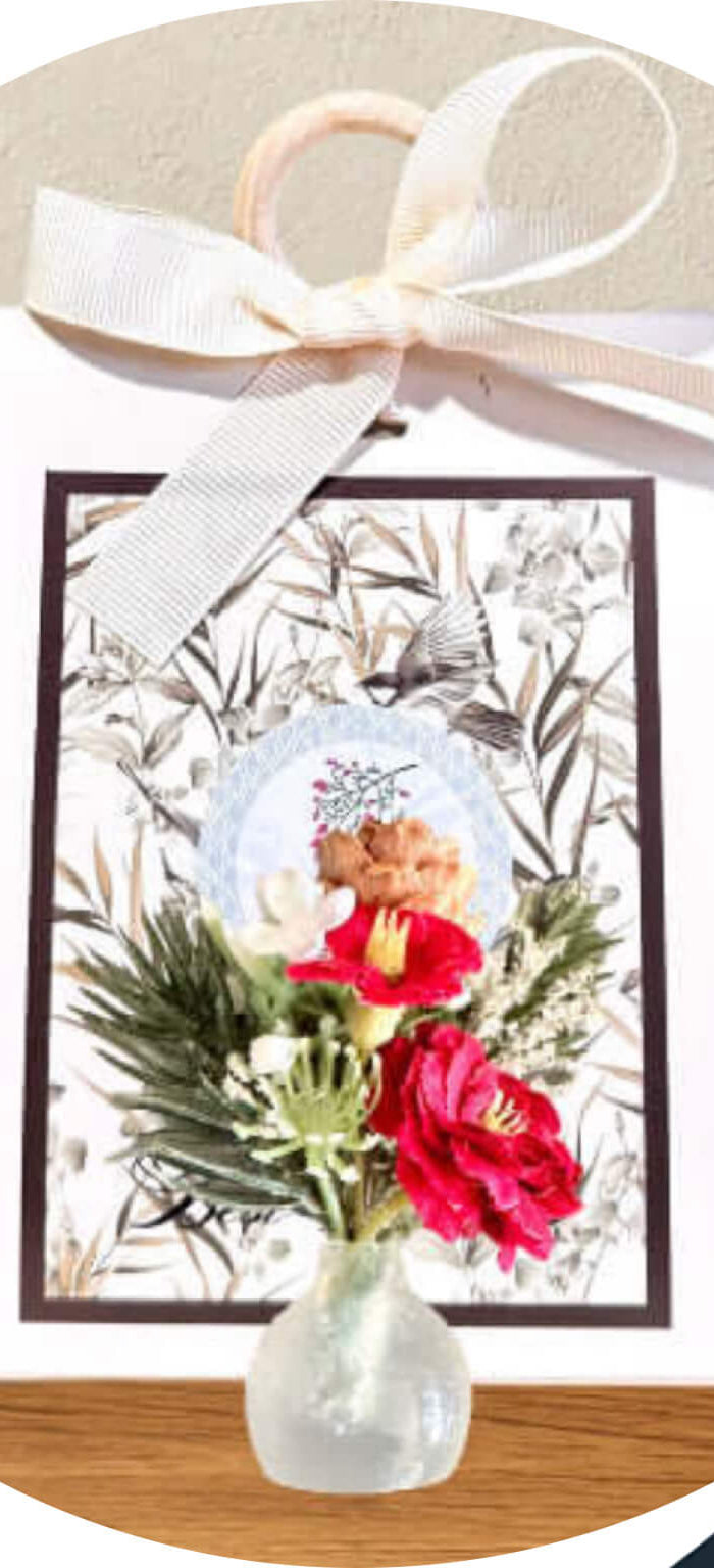 Floral arrangement in a vase with a decorative card on a wooden surface, surrounded by decorative elements.