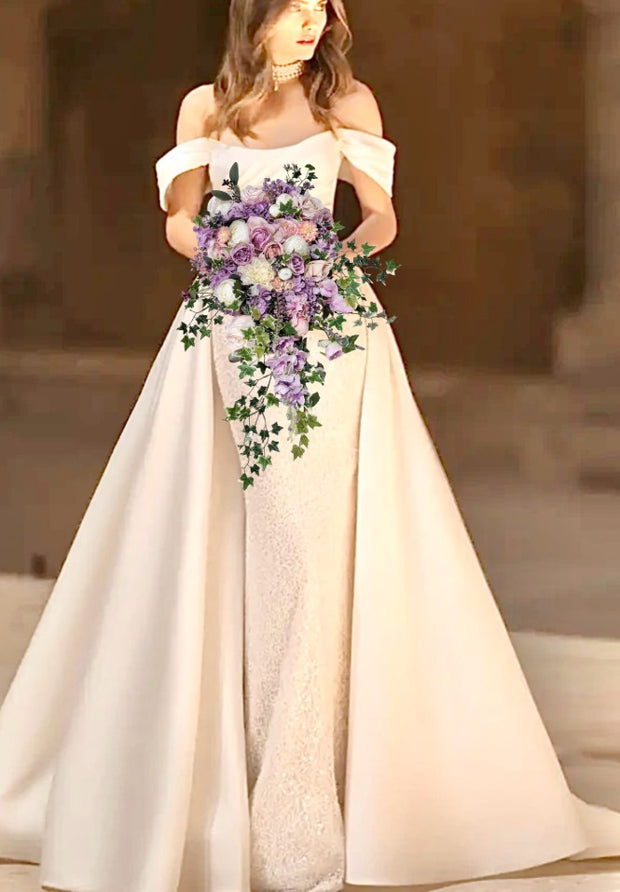 Woman in a white off-shoulder dress holding a bouquet of flowers against a blurred background